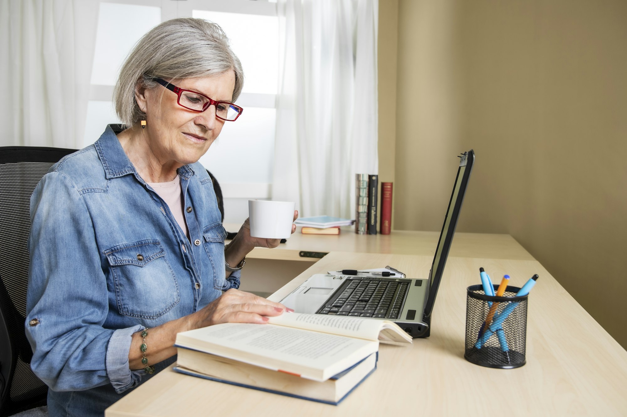 older woman studying with a laptop and books on a desk